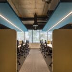 Un ambiente aziendale strutturato con postazioni ergonomiche e divisori per garantire concentrazione e produttività. Il soffitto industriale e i pannelli acustici blu conferiscono uno stile moderno e funzionale, ideale per team di lavoro focalizzati.