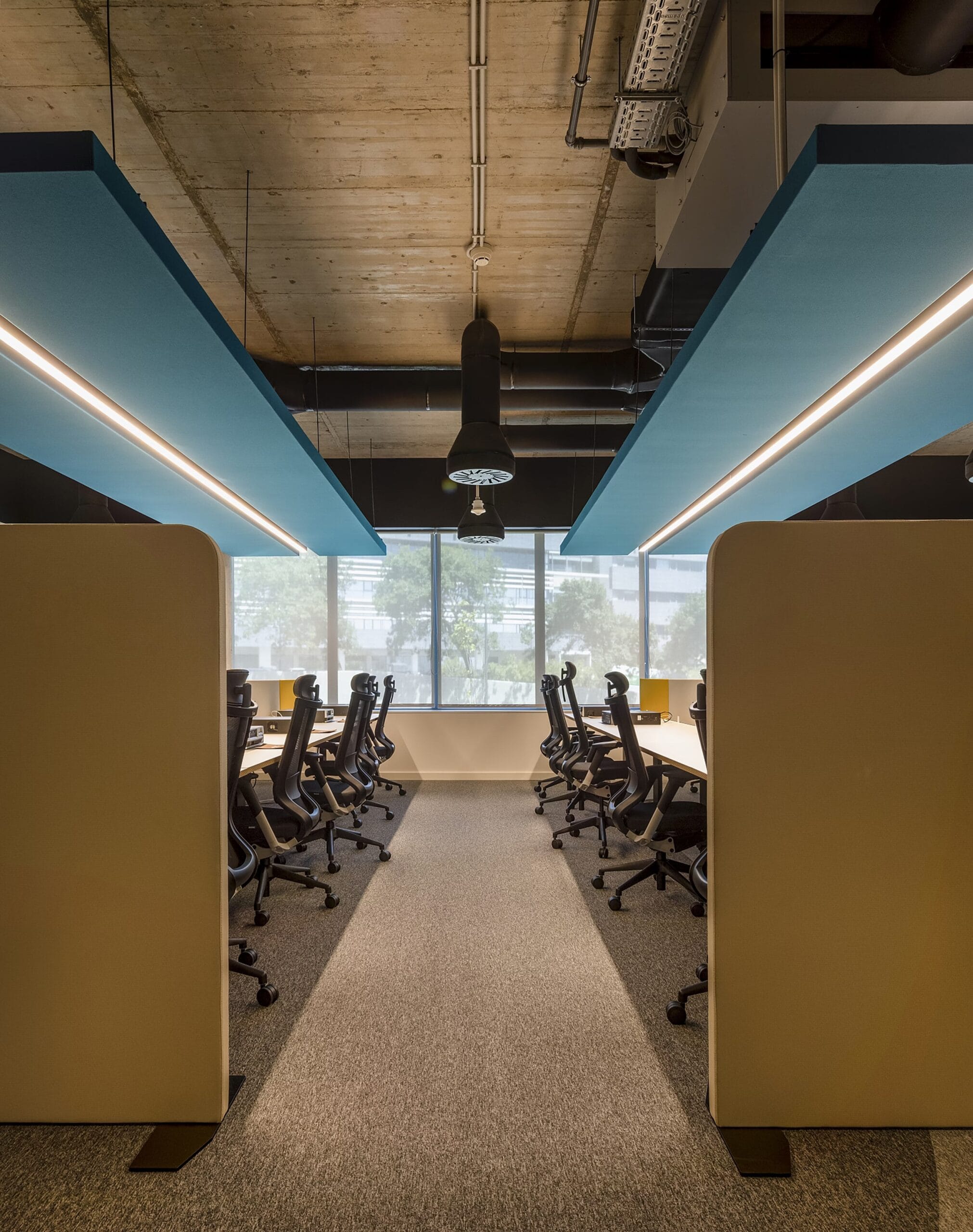 Un ambiente aziendale strutturato con postazioni ergonomiche e divisori per garantire concentrazione e produttività. Il soffitto industriale e i pannelli acustici blu conferiscono uno stile moderno e funzionale, ideale per team di lavoro focalizzati.