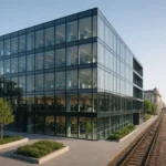 Centro direzionale moderno vicino a una stazione ferroviaria di Milano con facciata in vetro, architettura contemporanea e dettagli verdi esterni.