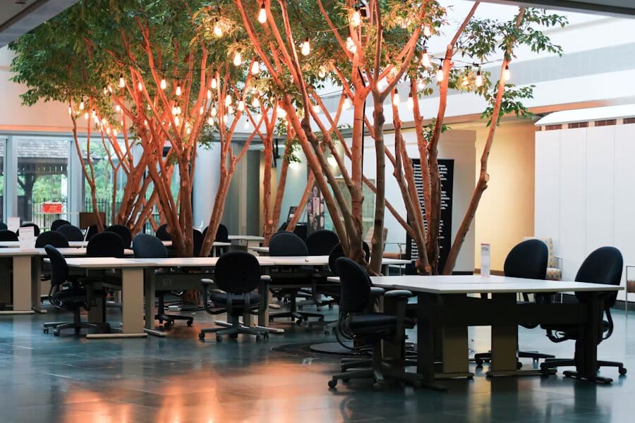 Spazio coworking con tavoli condivisi e alberi illuminati che crescono al centro della sala